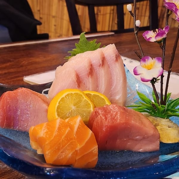 A vibrant Koryo Sushi sashimi platter with various fish, lemon slices, and decorative flowers.