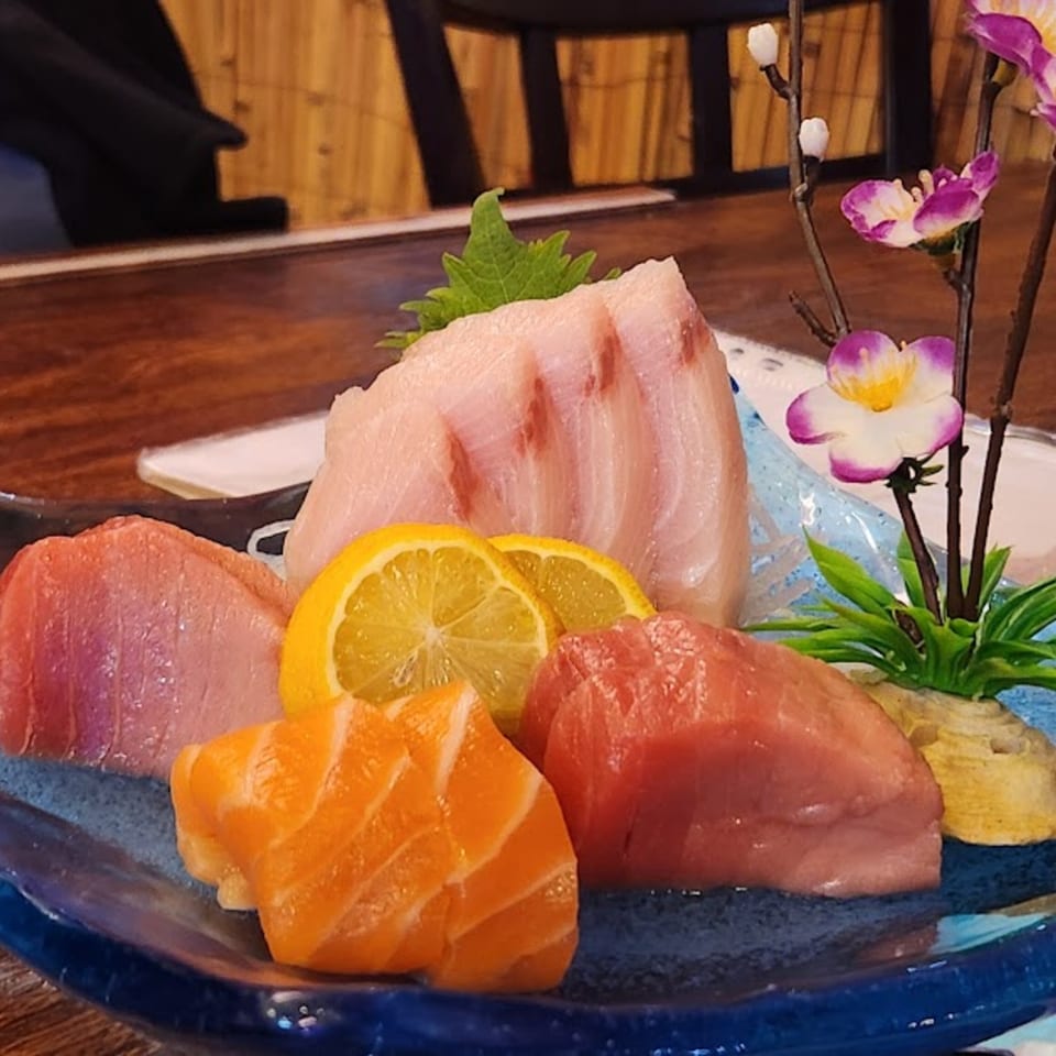 A vibrant Koryo Sushi sashimi platter with various fish, lemon slices, and decorative flowers.