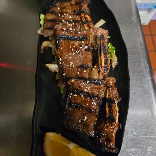 Grilled short ribs with sesame seeds, onions, and lettuce, served with an orange slice.