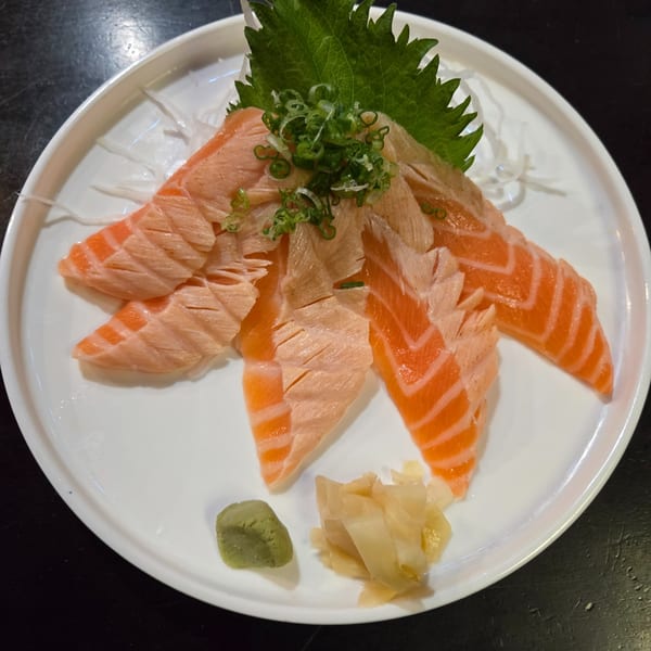 Koryo Sushi's salmon sashimi with green onions, wasabi, and pickled ginger on a white plate.