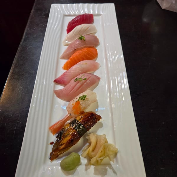 A long white plate holds various pieces of Koryo Sushi nigiri, including tuna, salmon, and eel.